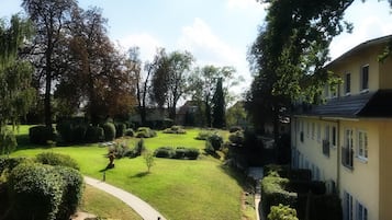 A well-maintained garden with a paved pathway, neatly trimmed hedges, and mature trees.