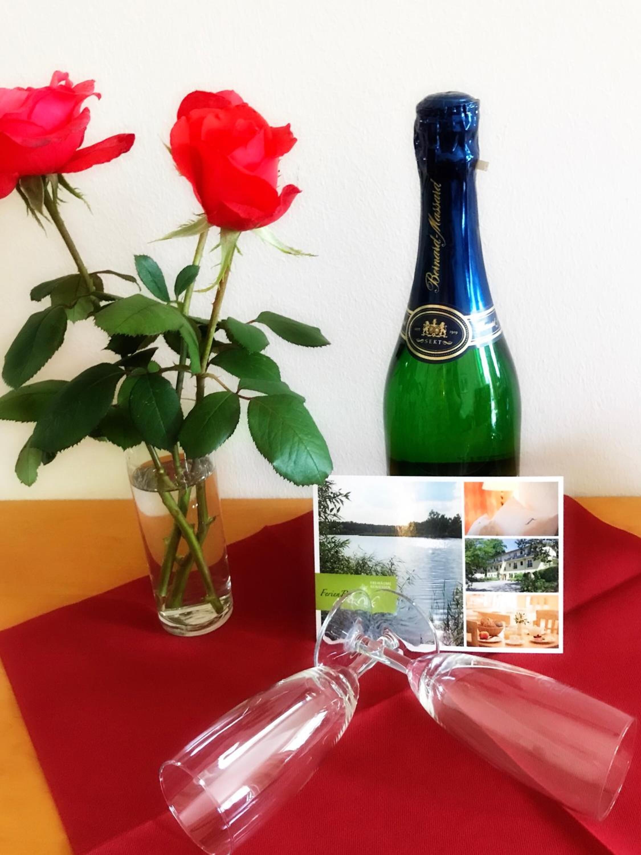 A table with a green bottle, two red roses, and a clear glass.