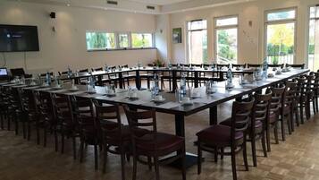 A conference room with long tables, chairs, and a large screen.