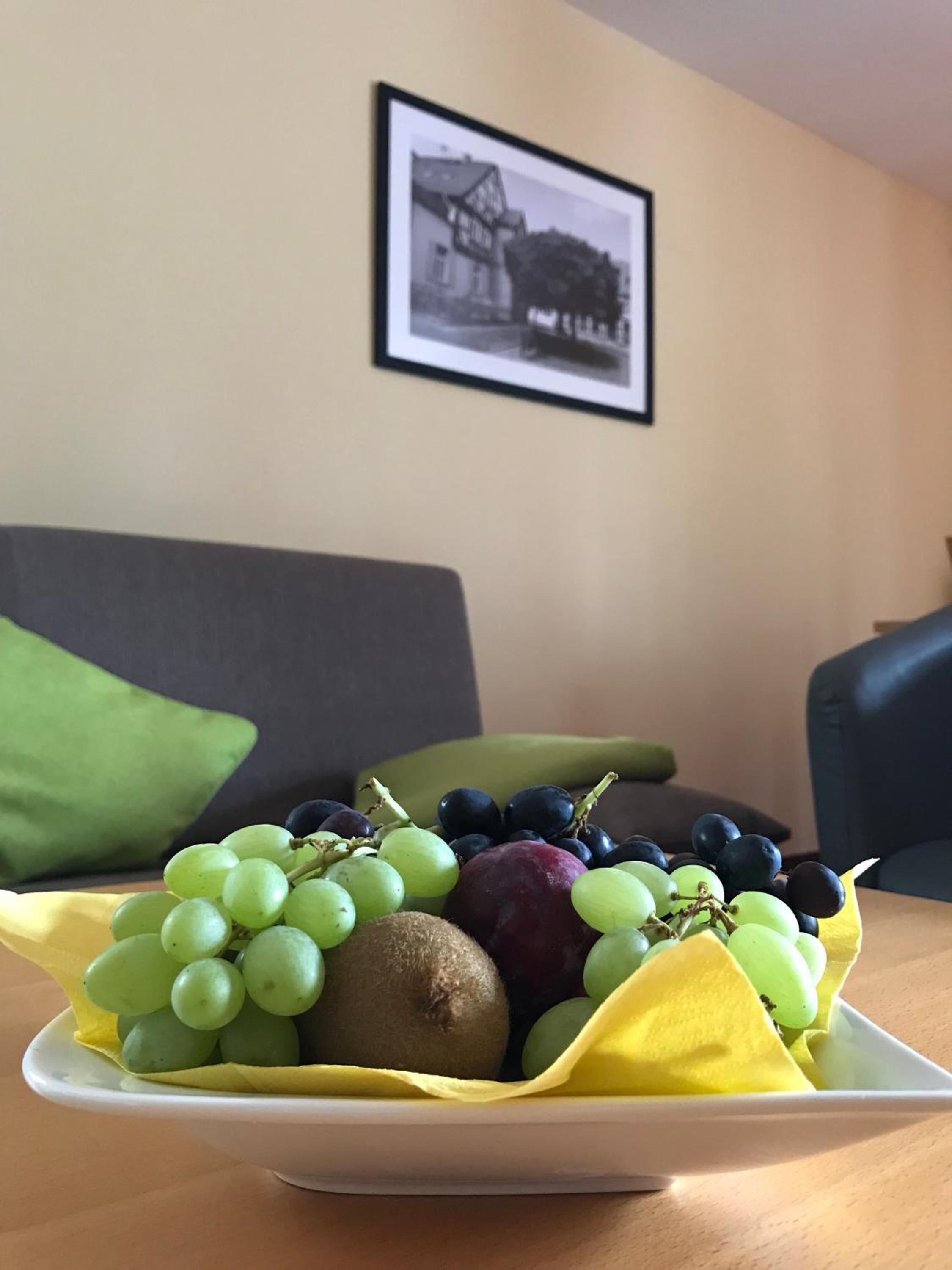 Eine Obstschale auf einem Tisch, im Hintergrund ein gerahmtes Bild an der Wand.