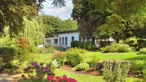 A white building with a covered porch, surrounded by a well-maintained garden with various flowering plants and a stone pathway. - FerienResidenz MüritzPark (Röbel/Müritz)