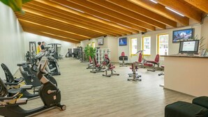 A gym with cardio machines, weightlifting equipment, and a reception area with a TV. - FerienResidenz MüritzPark (Röbel/Müritz)