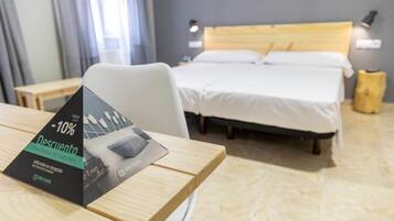 Et hotelværelse med en seng, et skrivebord og en stol. Der er et tilbudsskilte på skrivebordet.