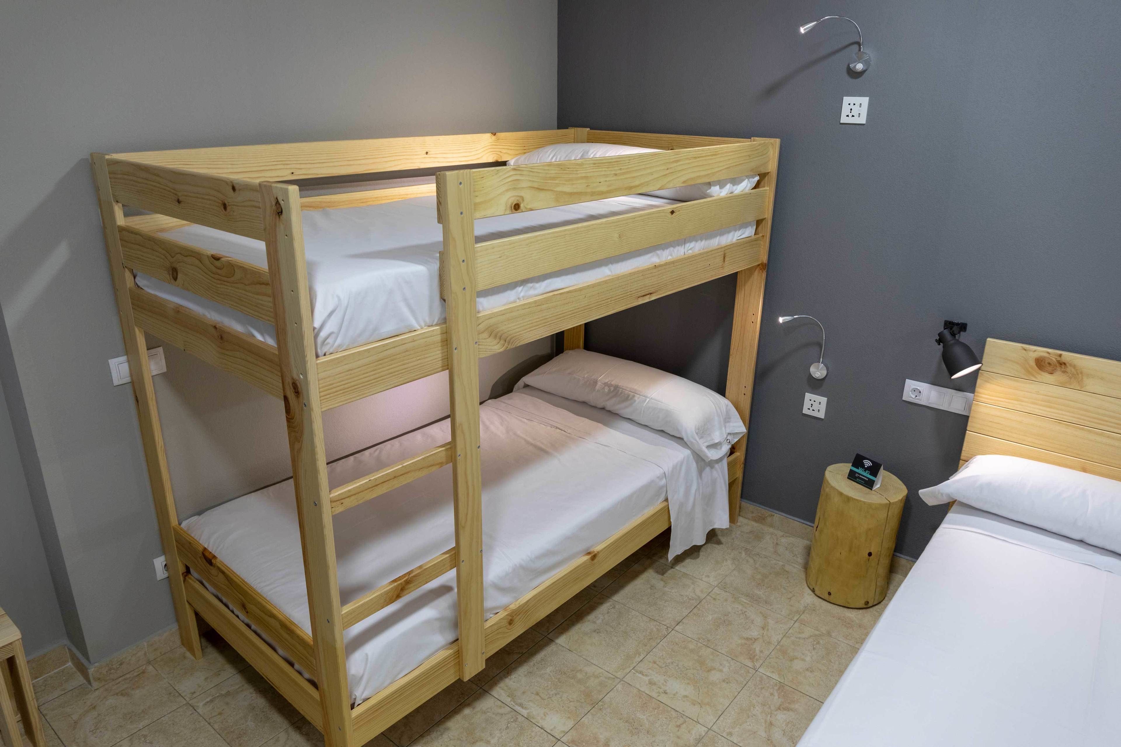 A bunk bed with two levels, a bedside table, a lamp, and a small wooden stool.