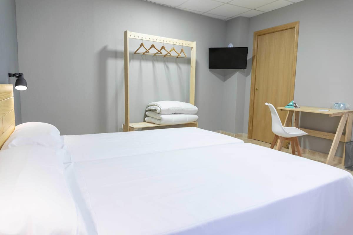 Une chambre d’hôtel comprenant un lit, un bureau, une chaise, une télévision et une armoire en bois.