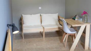A small, modern room with a wooden sofa, a dining table with chairs, and a lamp.
