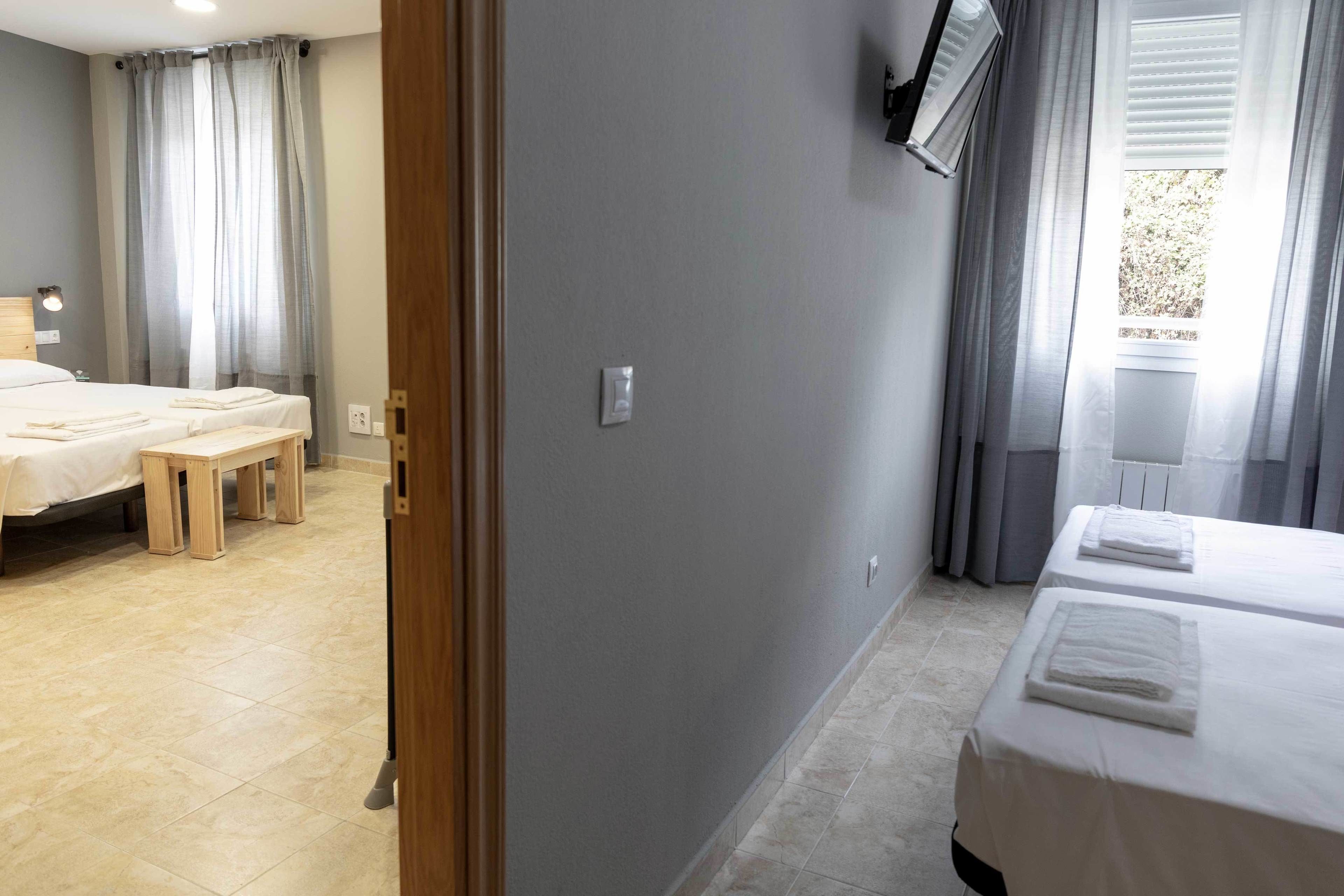 A hotel room with two beds, a bench, and a window with curtains.