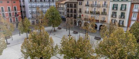 A square with trees and benches, surrounded by multi-story buildings with balconies and windows.