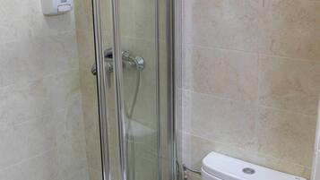 Un baño con ducha de vidrio, inodoro blanco y barra para toallas sobre el inodoro.