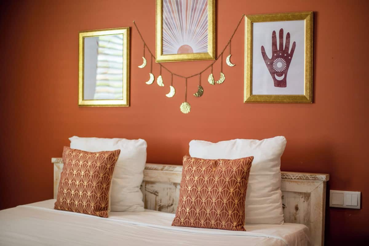 Un lit avec deux oreillers à motifs, une tête de lit et des éléments de décoration murale, notamment des tableaux encadrés et des ornements suspendus.