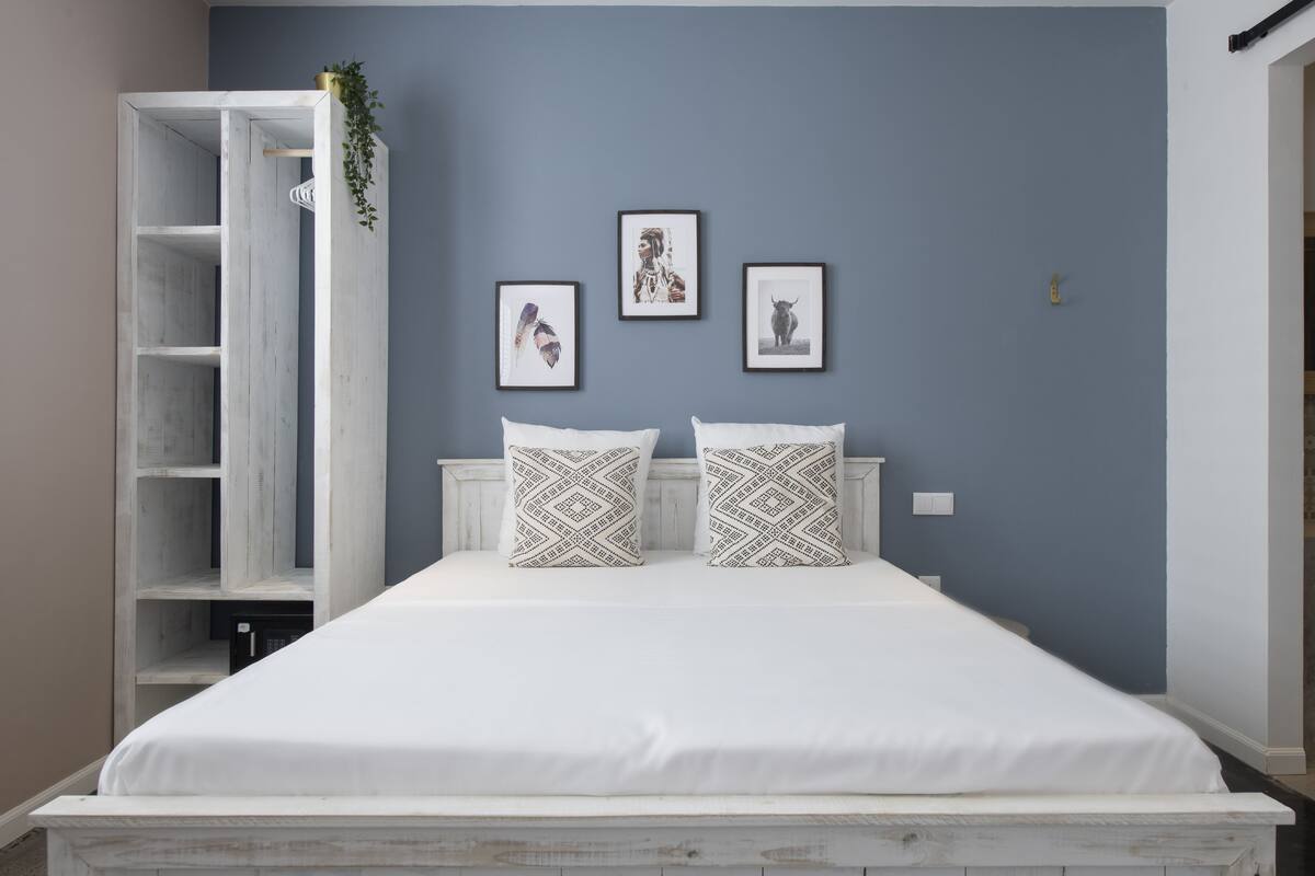 Une chambre à coucher avec un lit, une tête de lit blanche et deux oreillers. Trois tableaux encadrés sont accrochés au mur.