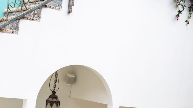 Zona de piscina con dos personas en traje de baño, una pared blanca y un farol colgante.