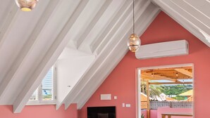 Un dormitorio con techo inclinado, una cama con manta estampada, un televisor y vistas a un patio exterior.