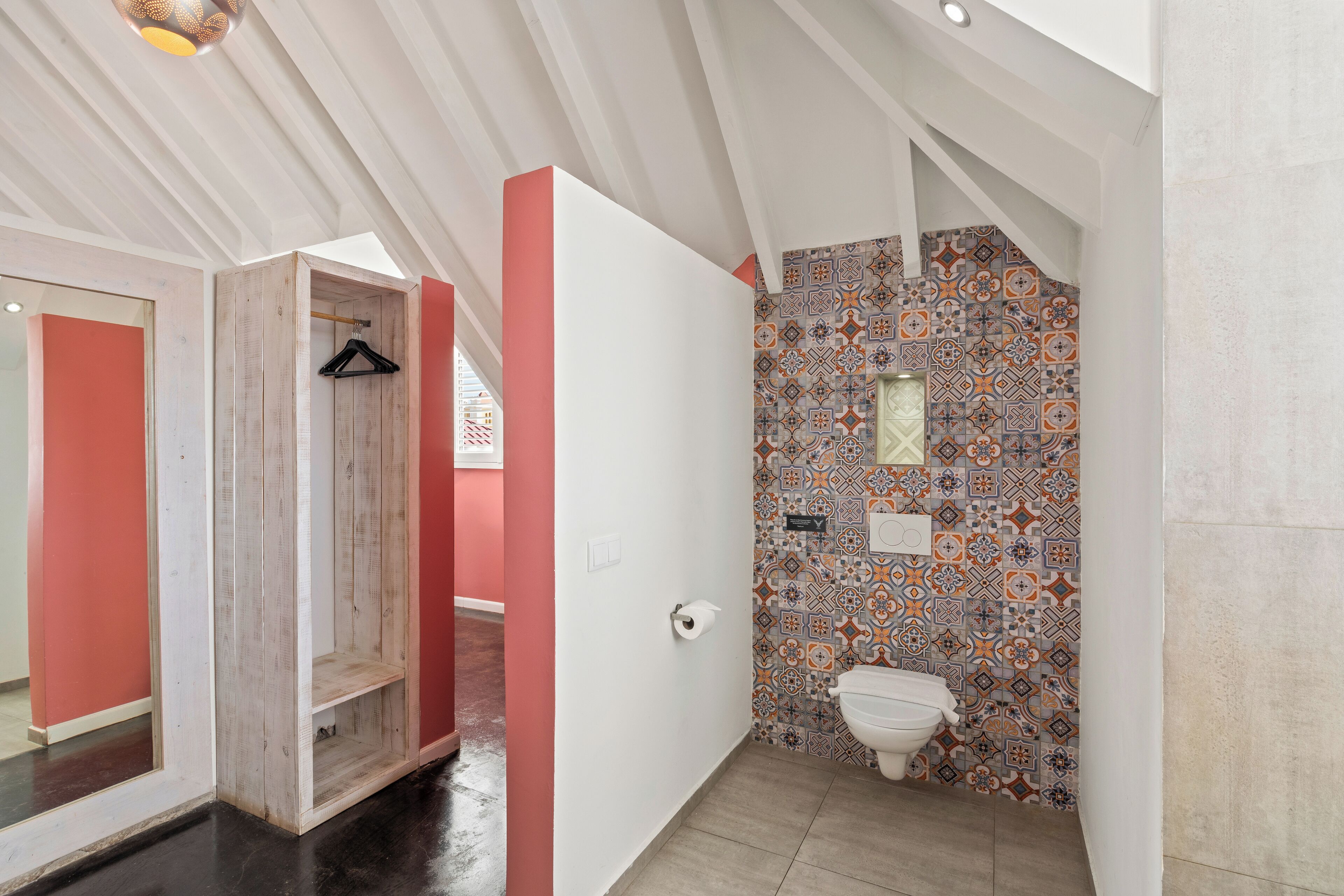 Casa de banho com parede revestida em azulejos, sanita e um suporte de madeira suspenso.