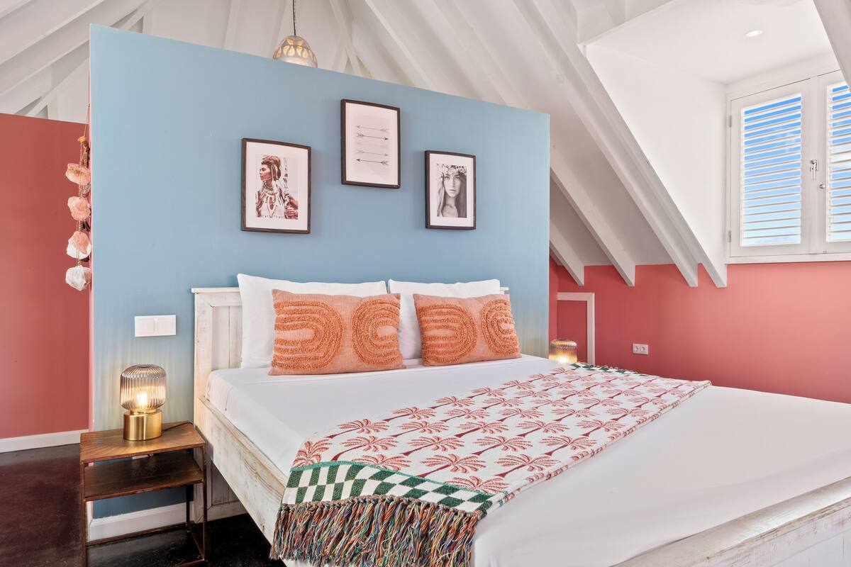 Une chambre à coucher avec un lit, une table de chevet, un mur orné de tableaux encadrés et une fenêtre avec des volets.