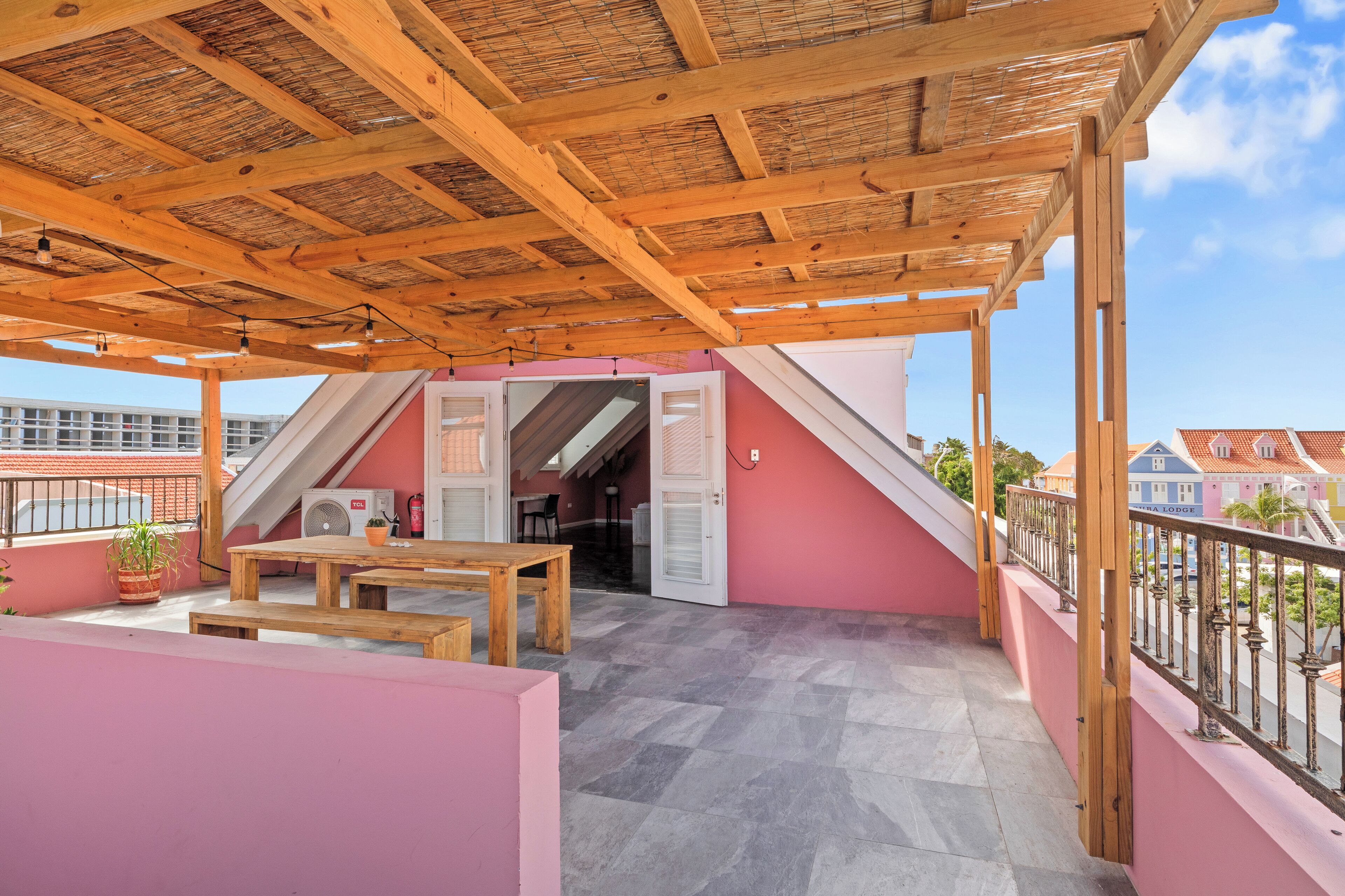 A covered outdoor area with a wooden ceiling, a pink wall, a table, and a bench.