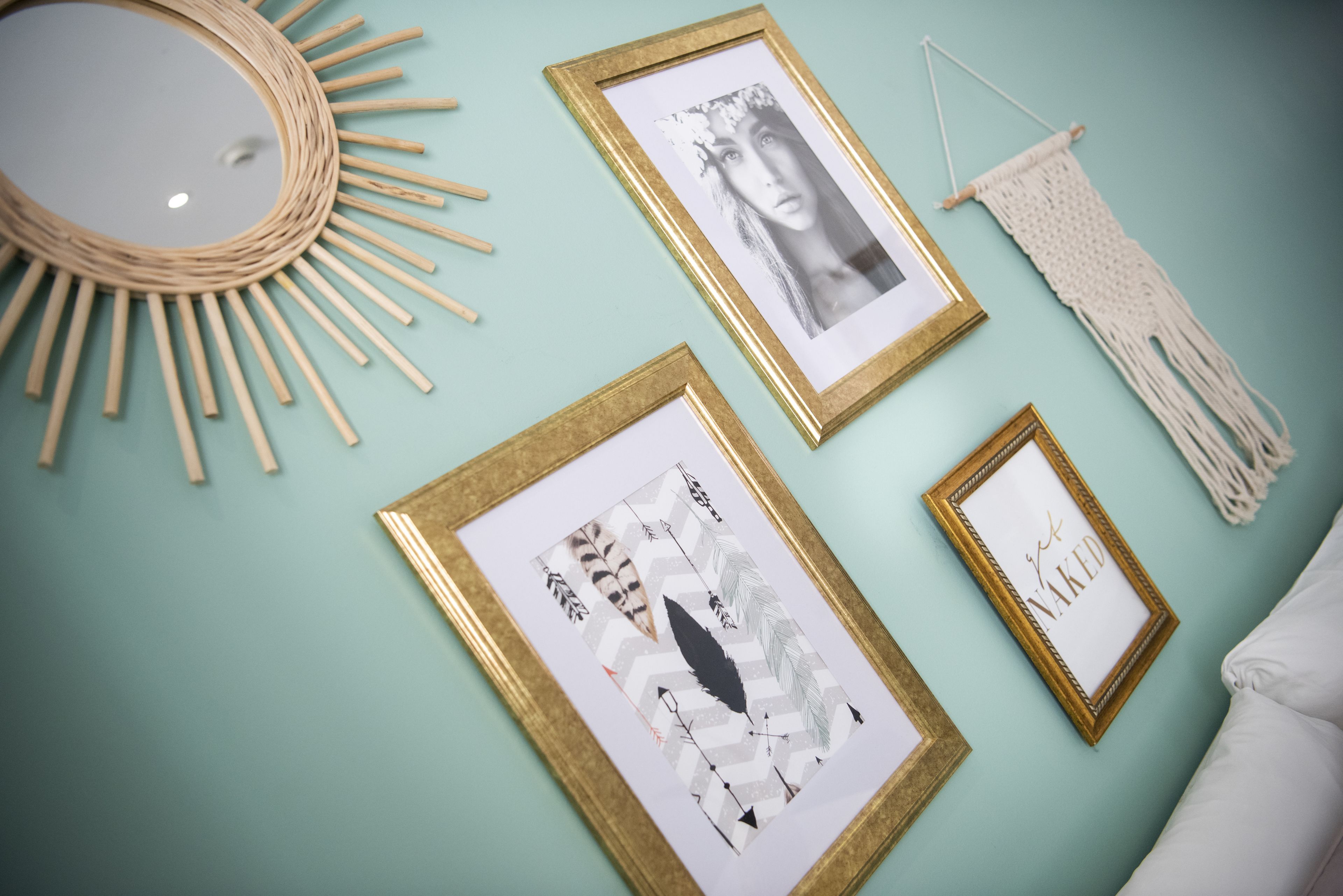 Una parete color petrolio con quattro opere d'arte incorniciate, una decorazione solare in fibre naturali e un arazzo in macramè.