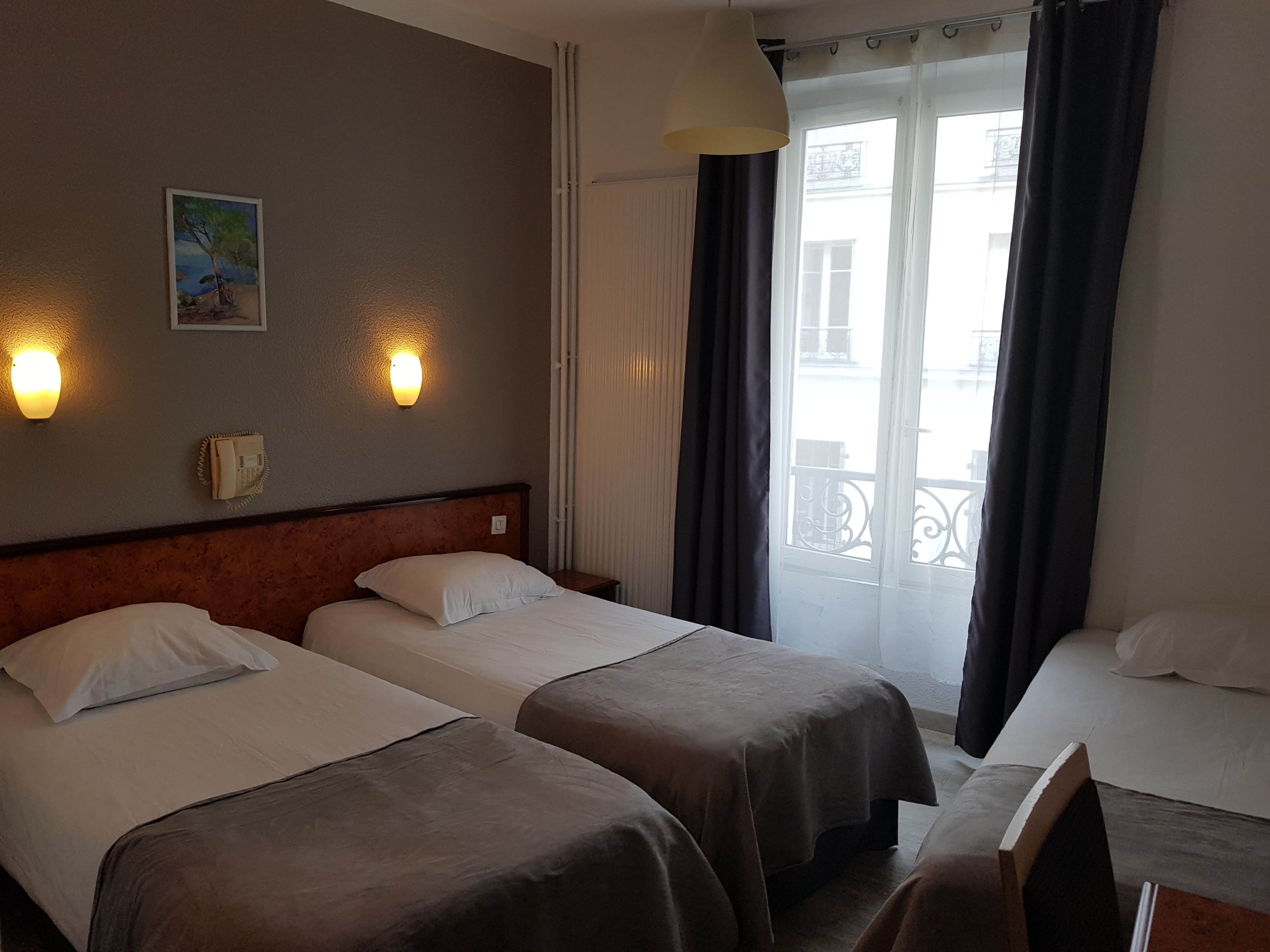 Habitación de hotel con dos camas individuales, cabecera de madera, un cuadro en la pared y una ventana con cortinas.