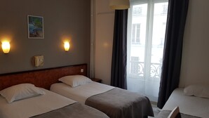 Habitación de hotel con dos camas individuales, cabecera de madera, un cuadro en la pared y una ventana con cortinas.