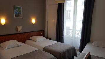 Habitación de hotel con dos camas individuales, cabecera de madera, un cuadro en la pared y una ventana con cortinas.