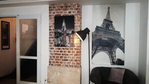 Una habitación con una pared de ladrillo, una puerta y dos carteles; uno de la Torre Eiffel y otro de un paisaje urbano.