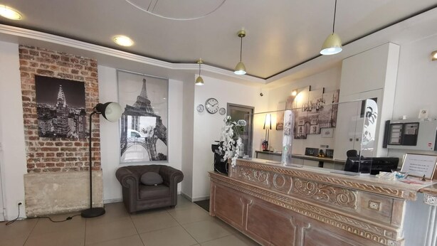 Un área de recepción con pared de ladrillo, un cartel grande de la Torre Eiffel, un sillón de cuero, una recepción con espejo y un reloj en la pared.