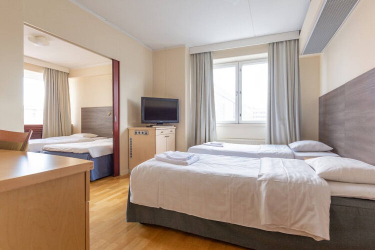 A hotel room with two beds, a desk, a television, and a window with curtains.