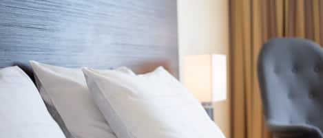 Un lit bien fait, avec une literie et des oreillers blancs, une tête de lit sombre et une chaise au fond de la pièce.