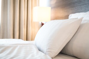 A neatly made bed with white bedding and pillows, a wooden headboard, and a lamp in the background. - Torget Hotel (Pori)