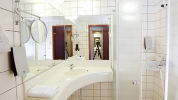 A modern bathroom with a large mirror, two sinks, and a shower.