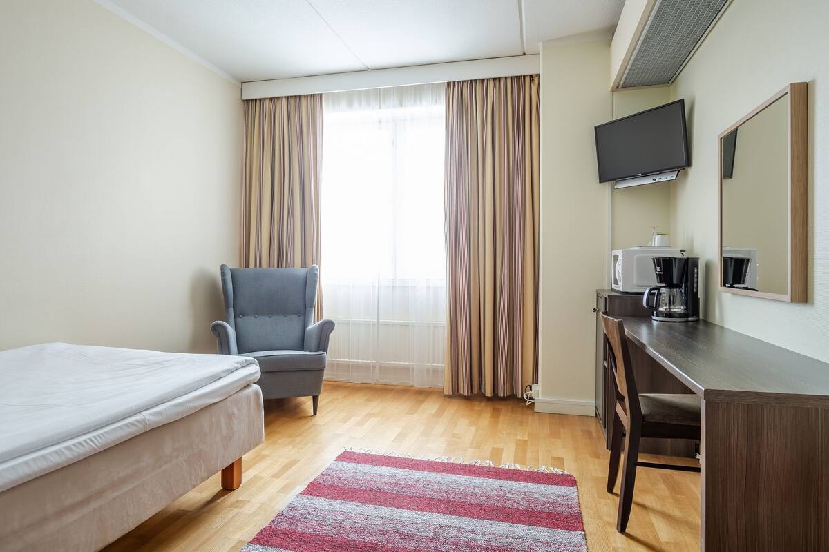 A hotel room with a bed, a desk, a chair, a television, and a coffee maker.