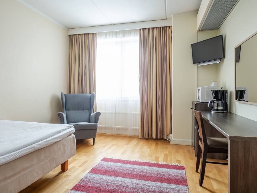 A hotel room with a bed, a desk, a chair, a television, and a coffee maker.
