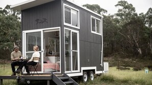 A modern, two-story cabin with a deck and a staircase leading to the entrance. - Saddle Camp Tiny House 2 by Tiny Away (Braidwood)