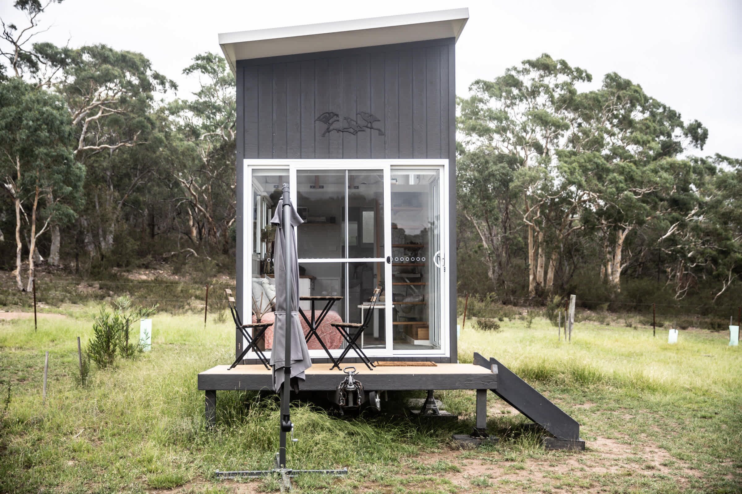 Une cabane moderne et compacte, dotée d’une porte-fenêtre, d’un petit espace extérieur avec des sièges et d’une terrasse en bois.