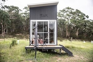 Eine moderne, kompakte Holzhütte mit Glastür, einer kleinen Außenlounge und einer Terrasse.