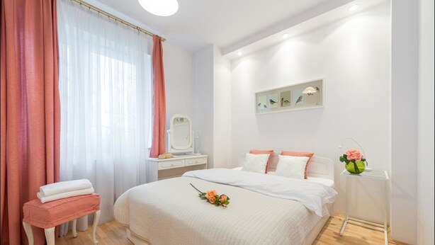 A bedroom with a large bed, a bedside table, a vanity with a mirror, and a small table with a vase of flowers. - P&O Apartments Grodkowska (Warsaw)