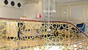 A hotel lobby with a high ceiling, a chandelier, a reception desk, and a seating area with red upholstered chairs and tables. - Hotel Kralice (Istanbul)