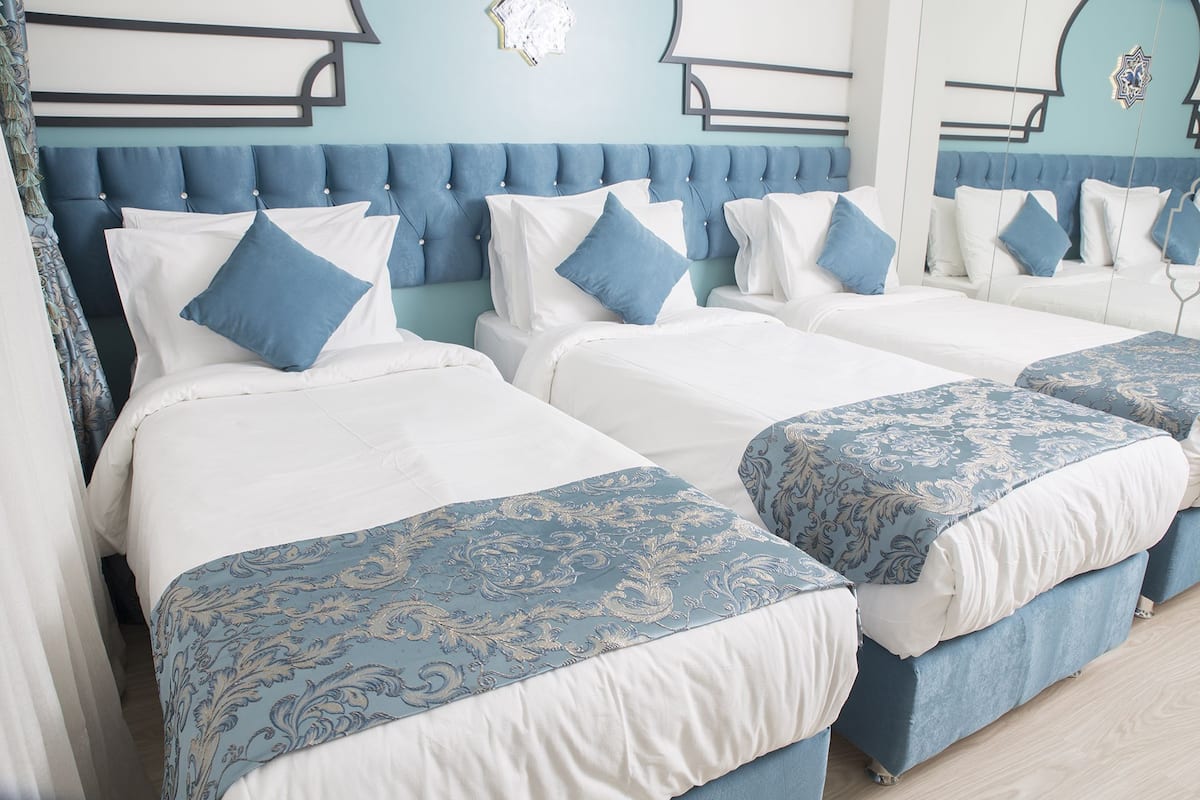 A hotel room with three beds arranged in a row, each with a blue headboard and white bedding.