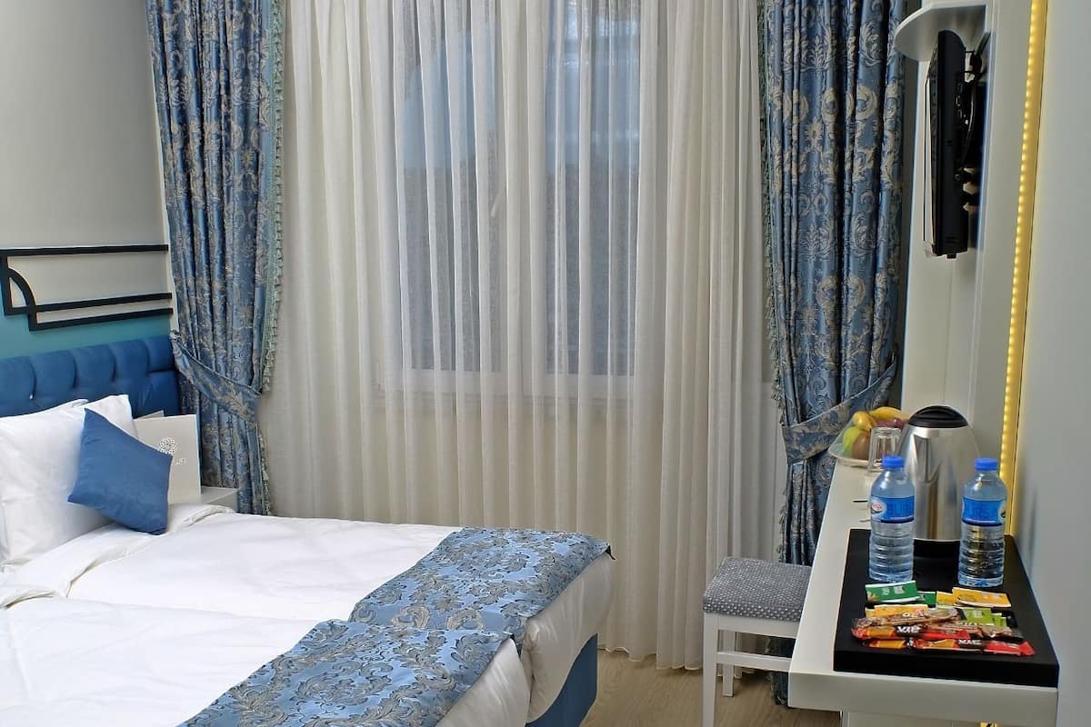 A hotel room with a bed, a desk with water bottles, a chair, and a suitcase.