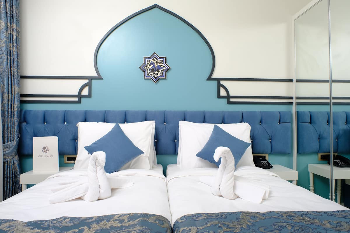 A hotel room with a large bed, two pillows, a wall-mounted artwork, a bedside table, and a mirror.