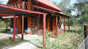 A rustic log cabin with a red roof, a porch with two lounge chairs, and a sign that reads "Refugio Familia". - Refugio Familiar (La Paloma)