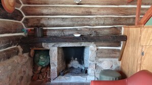 A stone fireplace with logs, a red leather chair, and a wooden shelf with various items. - Refugio Familiar (La Paloma)
