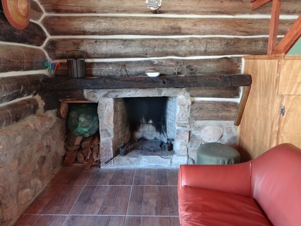 A stone fireplace with logs, a red leather chair, and a wooden shelf with various items.
