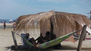 A beach hut with a thatched roof, a hammock, and a beach chair. - Refugio Familiar (La Paloma)