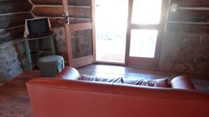 A log cabin interior with a red leather sofa, a television on a small table, and a stone wall. - Refugio Familiar (La Paloma)