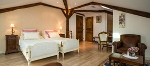 Un dormitorio con dos camas, vigas de madera, una silla y una mesita con flores.