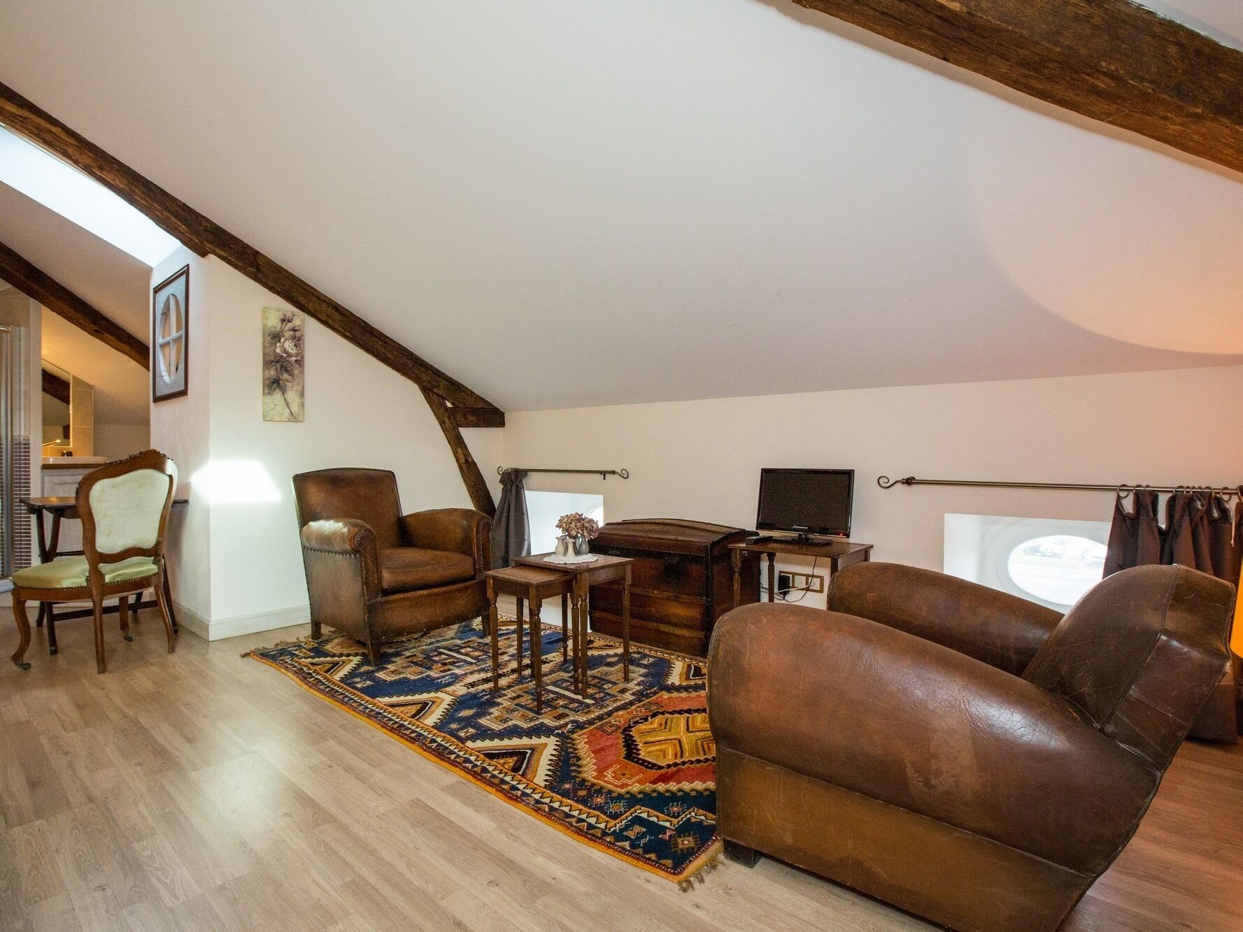 Un salon chaleureux de style loft, doté d’un haut plafond, de poutres apparentes, d’une grande fenêtre et d’un téléviseur.