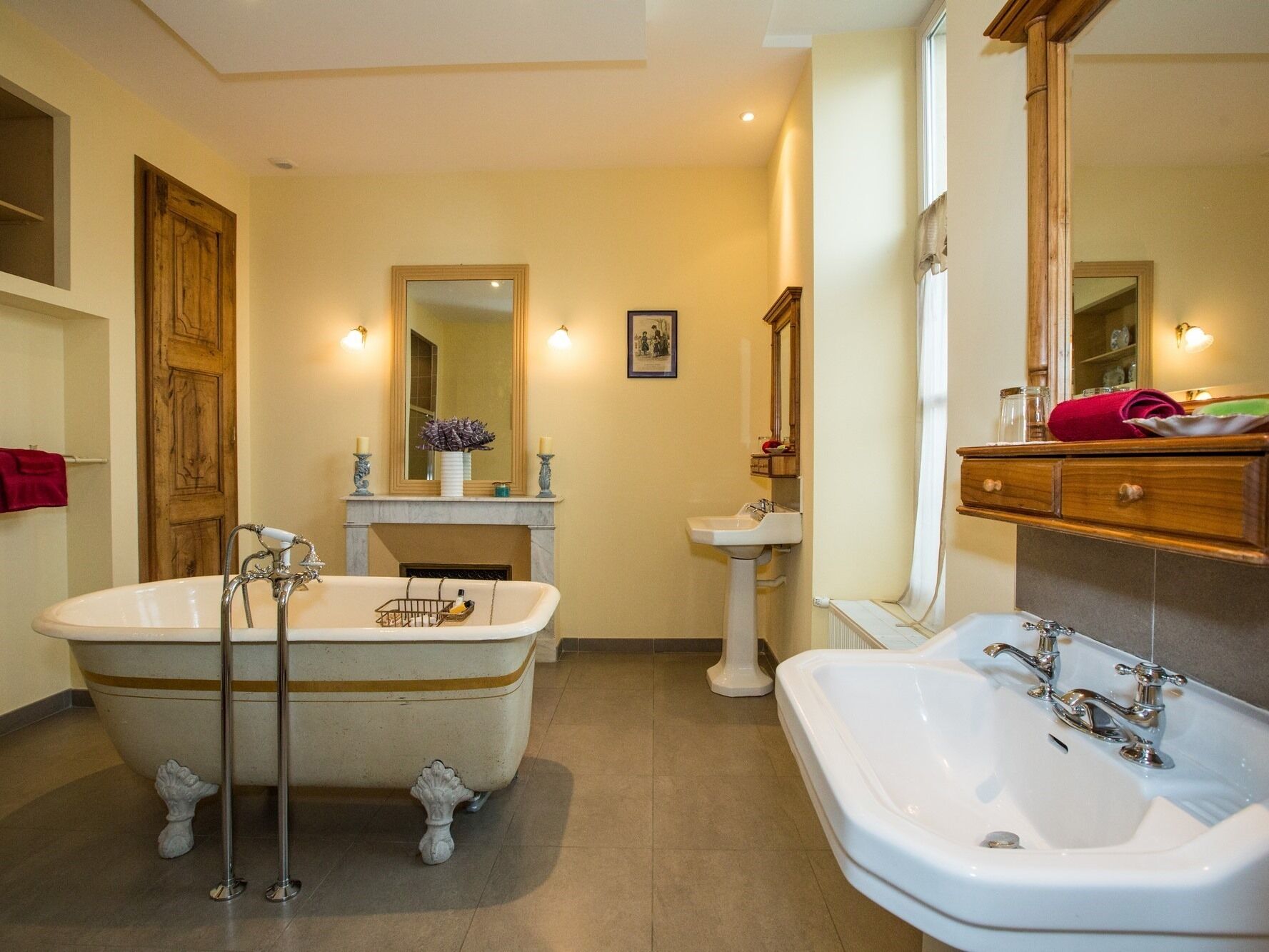 Une salle de bain avec une baignoire sur pieds, un lavabo sur colonne et une coiffeuse avec un miroir.