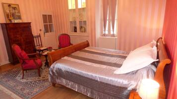 A bedroom with a bed, a chair, a desk, a dresser, and a window with curtains.
