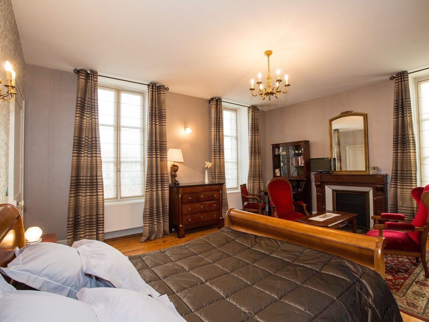 Een slaapkamer met een groot bed, een bureau, een stoel, een open haard en een spiegel.